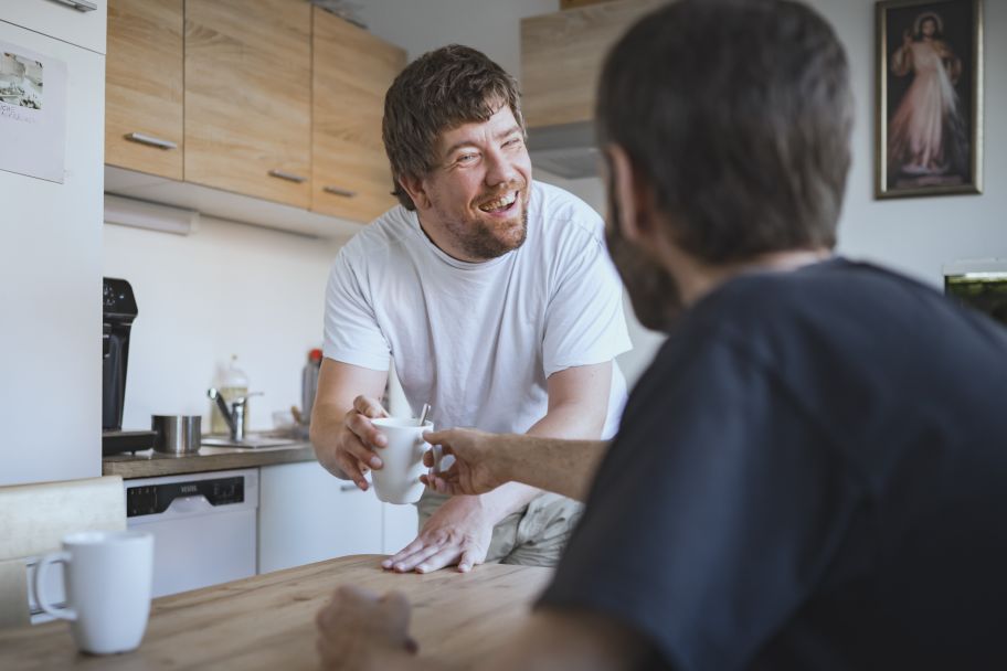 Zwei junge freundliche Männer beim Frühstückstisch helfen sich bei der Zubereitung von Kaffee.