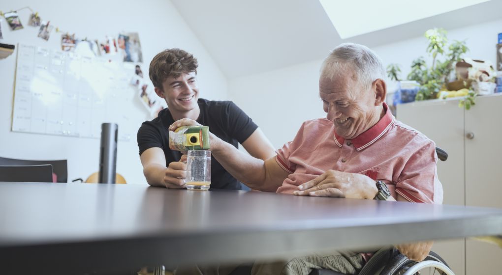 Ein Klient schenkt sich mit Hilfe seines Unterstützers Orangensaft ins Glas ein. 