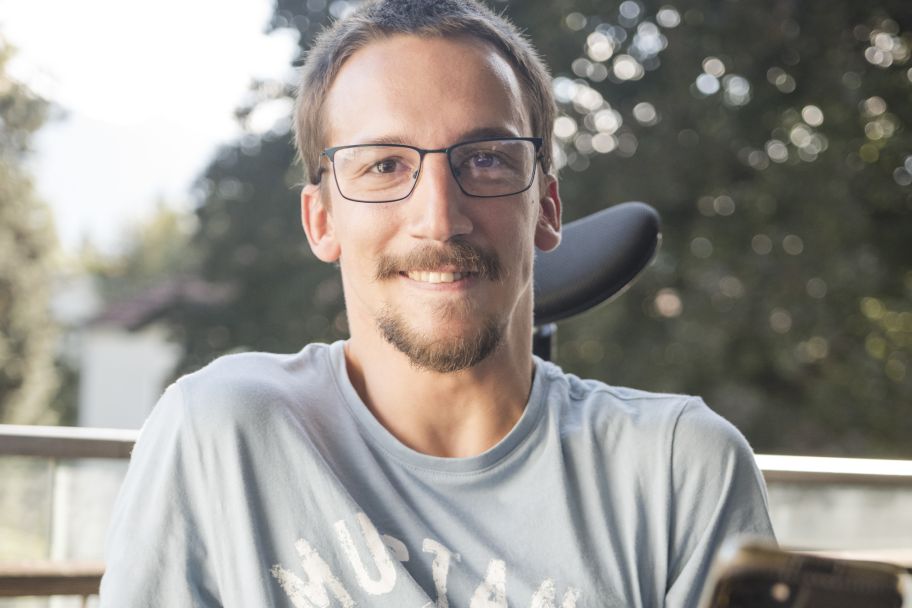 Ein junger Mann mit Spasmus lächelt in die Kamera