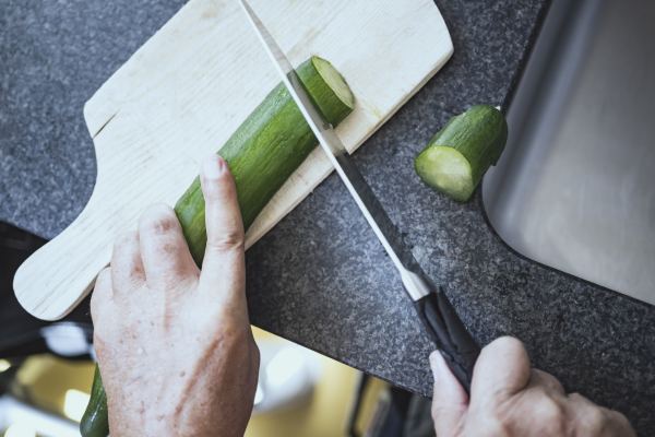 Vogelperspektive: eine Hand hält eine Salatgurke, die andere ein Messer; die Gurke wird in Scheiben geschnitten