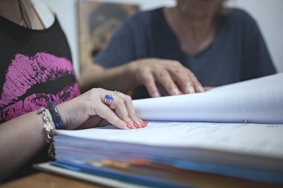 eine Frau mit lackierten Fingernägeln blättert in einem Ordner mit Dokumenten