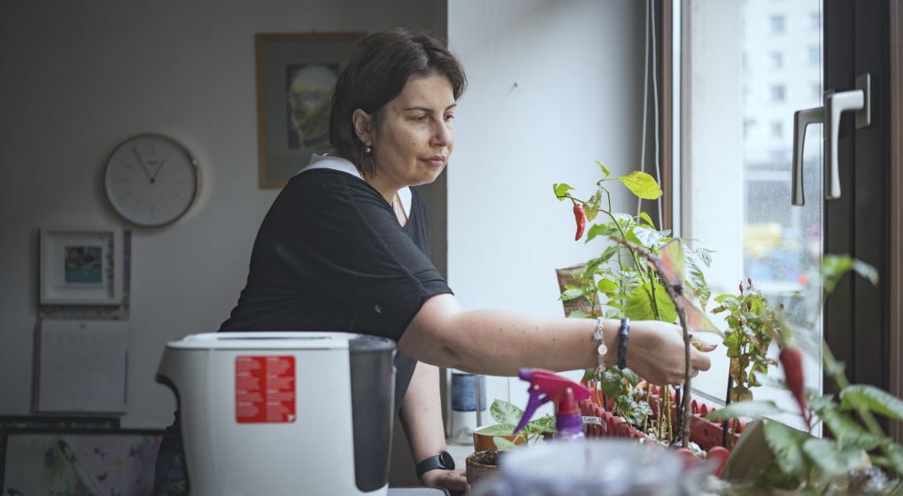 eine Frau steht an einem Fenster und kümmert sich um Pflanzen, die am Fensterbrett stehen