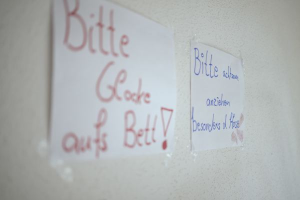 zwei Zettel an der Wand; an einem steht: "Bitte achtsam anziehen besonders die Hose"