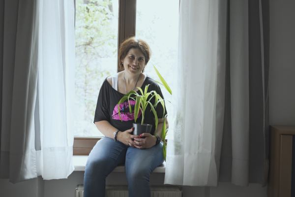 eine Frau sitzt auf einem Fensterbrett, sie hält eine Topfpflanze in den Händen