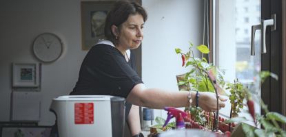 Frau steht an einem Fenster und pflegt Pflanzen