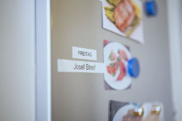 mit Magneten sind kleine Zettel an einem Kühlschrank befestigt; auf den Zetteln steht: Josef Streif; daneben ein Bild von einem Tomaten-Mozzarella Salat